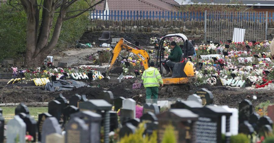 Mitarbeiter heben mit einem Bagger auf einem Friedhof in Nordengland neue Gräber aus.