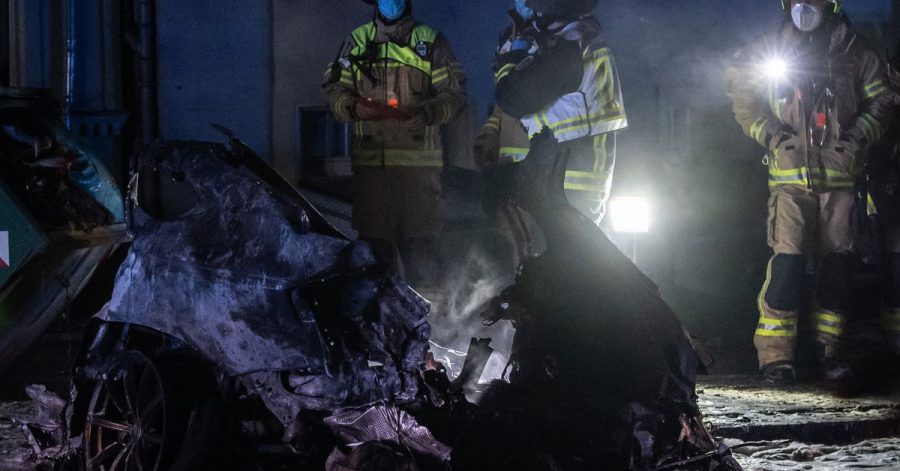 Einsatzkräfte der Feuerwehr stehen am Treptower Park neben dem Autowrack.