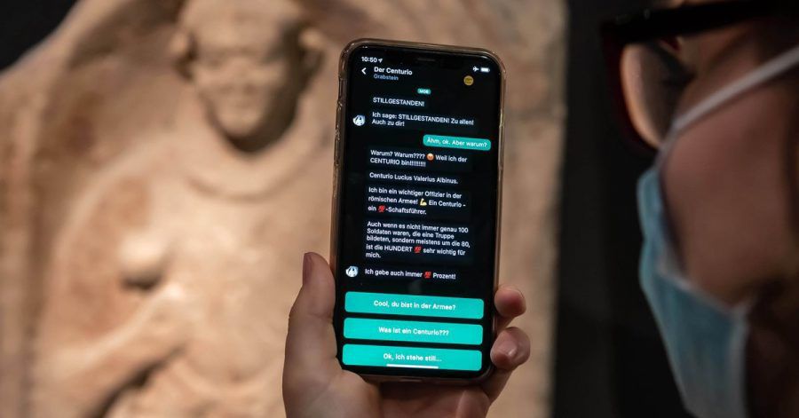 Im Badischen Landesmuseum wird vor einem Grabstein eines Centurio aus dem 1. Jahrhundert nach Christus auf einem Smartphone eine App gezeigt, mit der Museumsbesucher Kontakt zu Ausstellungsobjekten aufbauen können.