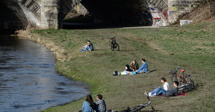 Junge Menschen genießen am Ufer der Leine in Göttingen das milde Wetter.