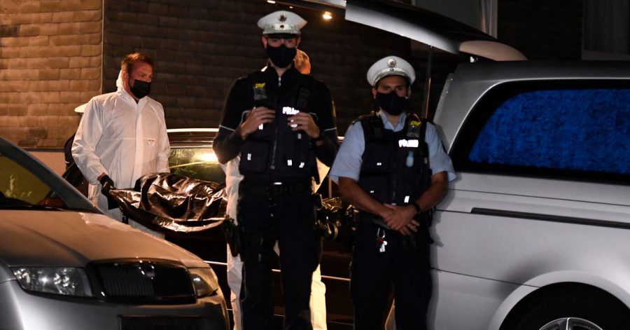 Mitarbeiter einer Beerdigungsfirma tragen eine Leiche unter Schutz von Polizisten zu einem Leichenwagen.