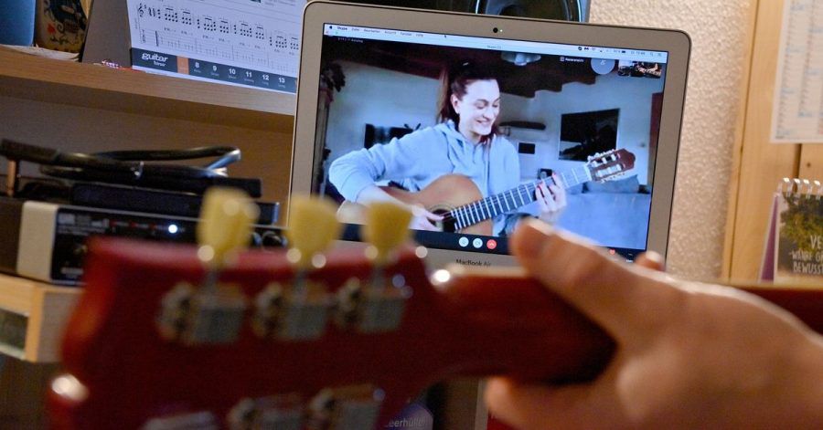 Ein Gitarrenlehrer unterrichtet eine Schülerin via Online-Videokonferenz.