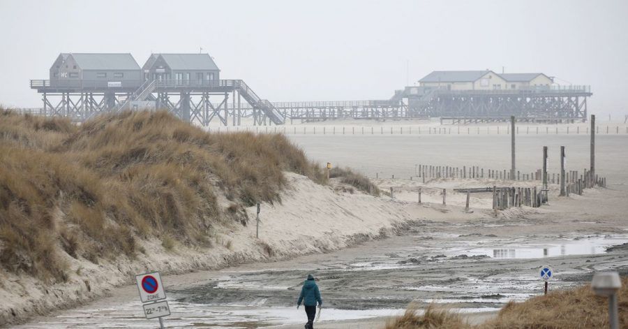 Eine Spaziergängerin ist bei regnerischem und windigem Wetter am Strand von St. Peter-Ording unterwegs. Nach Angaben des Deutschen Wetterdienstes werden an der Nordsee Böen mit Windgeschwindigkeiten bis zu 110 km/h erwartet.