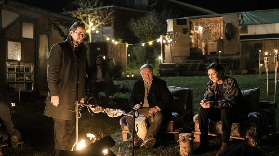 "Tatort: Rhythm and Love": Prof. Boerne (Jan Josef Liefers) und Kommissar Thiel (Axel Prahl) sitzen mit Inès Fournier (Maelle Giovanetti, v.l.) am Lagerfeuer. (dr/spot)