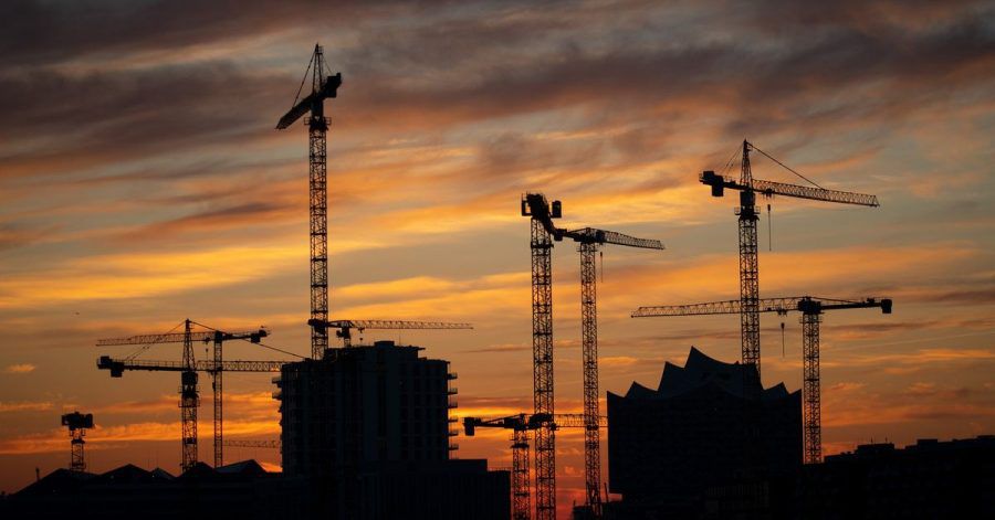 Die Kräne verschiedener Baustellen in der Hafencity zeichnen sich im Sonnenuntergang ab.