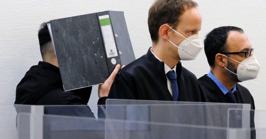 Der Angeklagte verbirgt im Sitzungssaal des Landgerichts Ingolstadt sein Gesicht hinter einem Aktenordner. Davor stehen seine Verteidiger.