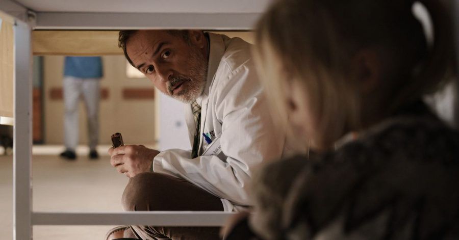 Doktor Ballouz (Merab Ninidze) kümmert sich um das Mädchen Flori (Mavie Meschkowski), das sich unter einem Tisch verkrochen hat.