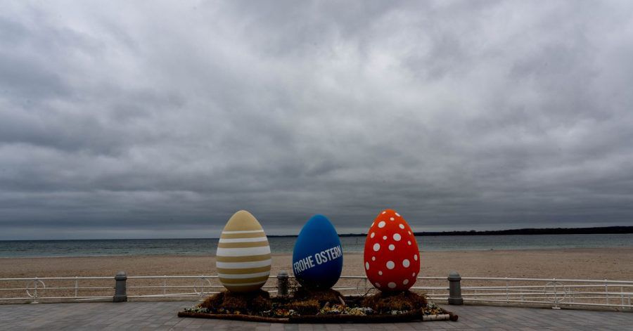 Bunt bemalte überdimensionale Ostereier stehen am wolkenverhangenen Strand von Travemünde.