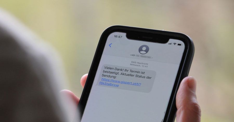 Eine Frau hält ein Smartphone in ihrer Hand, auf dessen Display eine Betrugs-SMS zu lesen ist.
