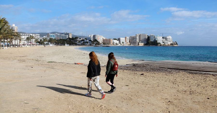 Zwei junge Frauen gehen am leeren Strand von Magaluf entlang.