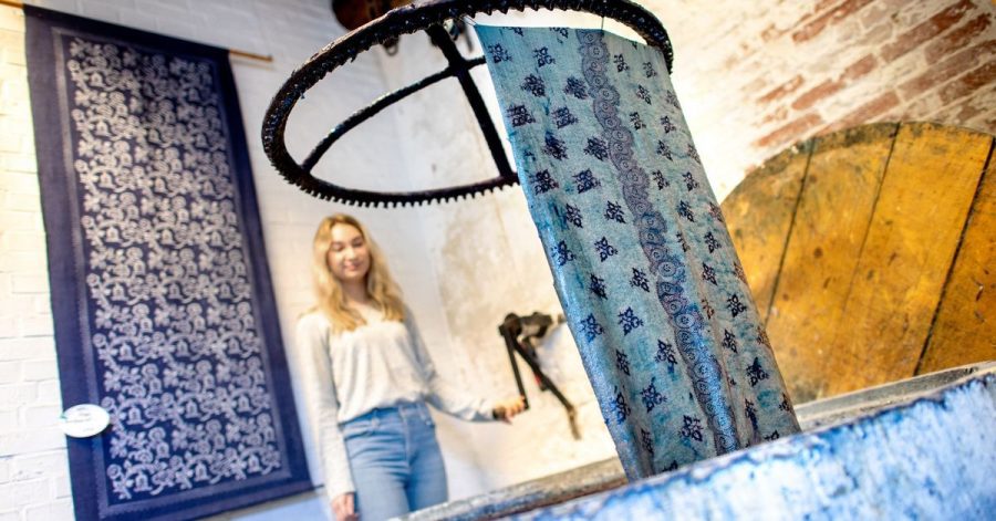 Blaudruckerin Sabrina Schuhmacher zieht den gefärbten Leinenstoff aus der sogenannten Küpe, einem Bottich mit blauer Indigo-Lösung, heraus.