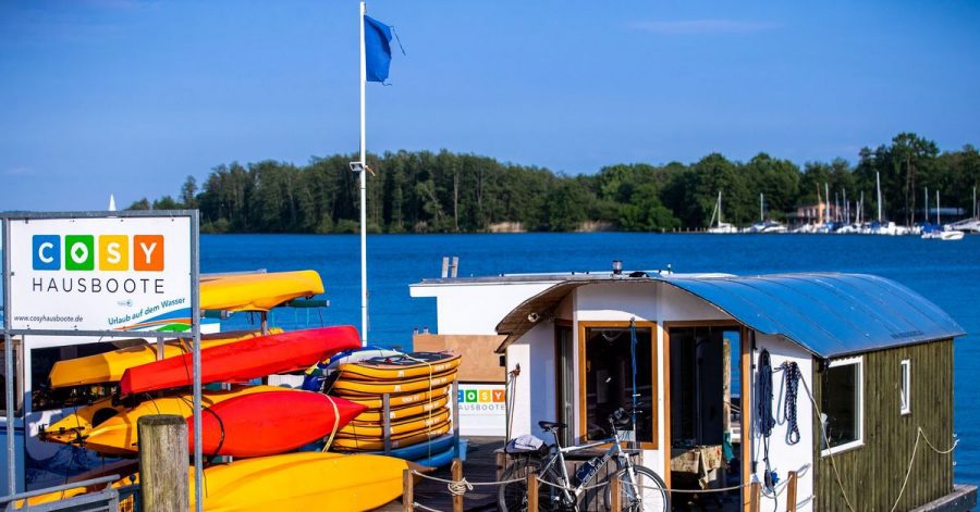 Ein Hausboot und Paddelboote liegen an einem Steg vor dem Schweriner Schloss.