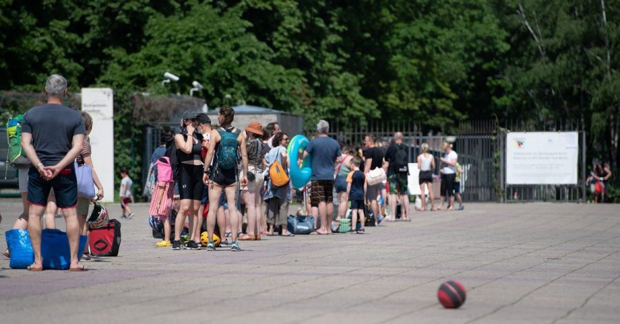 Menschen stehen bei warmem Wetter in einer Schlange vor dem Eingang zum Olympiabad in Berlin.