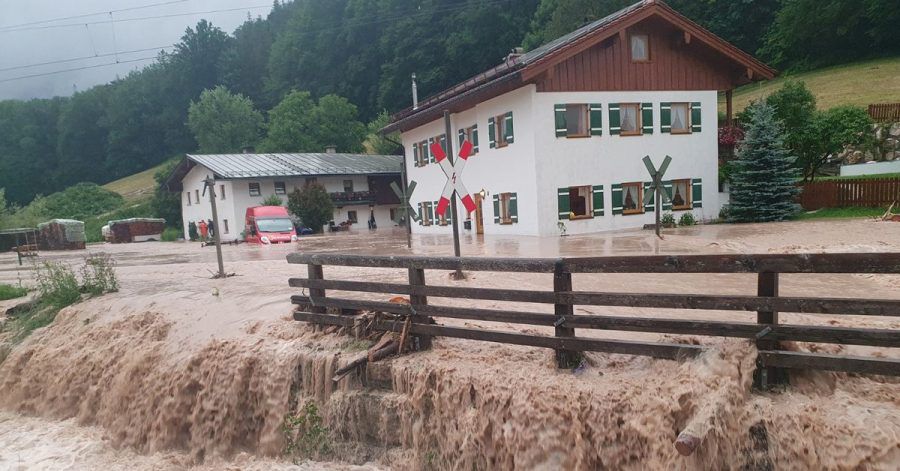 Wasser fließt über einen Platz vor einem Haus. Der Landkreis Berchtesgadener Land hat nach starkem Regen wegen Hochwassers den Katastrophenfall ausgerufen.