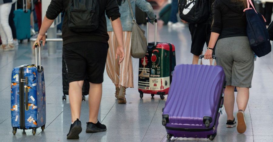 Reisende gehen im Flughafen Düsseldorf mit Koffern durch die Abflughalle.