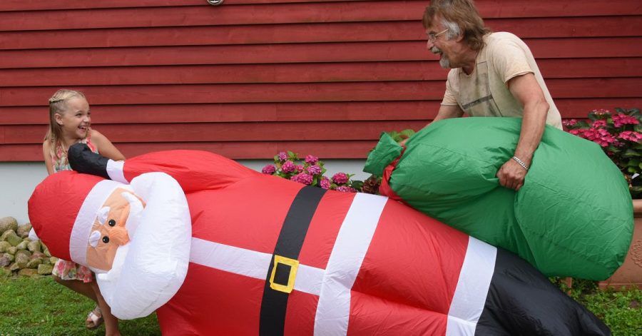 Lachend tragen Alicia und ihr Opa Dietmar Sawatzke den drei Meter großen aufgeblasenen Weihnachtsmann neben die mit Sommerblumen dekorierte Eingangstür.