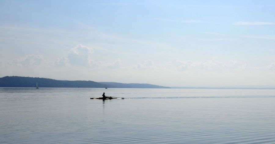 Ein Ruderer fährt bei Sonnenschein über den Starnberger See (Oberbayern).