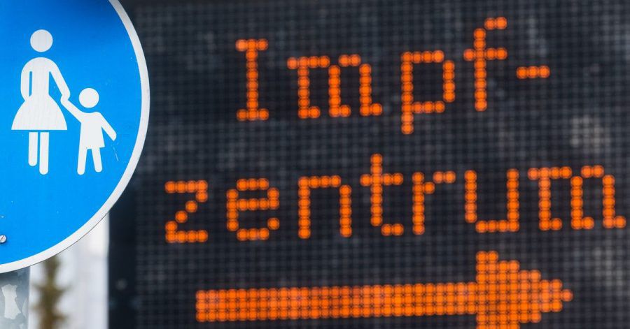 Eine elektronische Anzeigetafel mit dem Wort «Impfzentrum» hinter einem Verkehrsschild «Sonderweg Fußgänger» weist den Weg zu einem Impfzentrum.