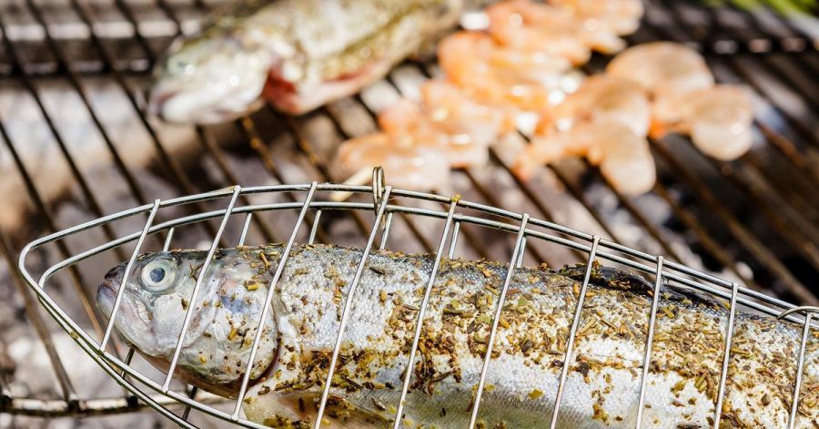 Die Forelle brutzelt in der Fischzange. So kommt sie nicht mit dem Rost in Berührung. Und damit die Garnelen nicht in die Glut fallen, stecken sie auf einem Holzspieß.