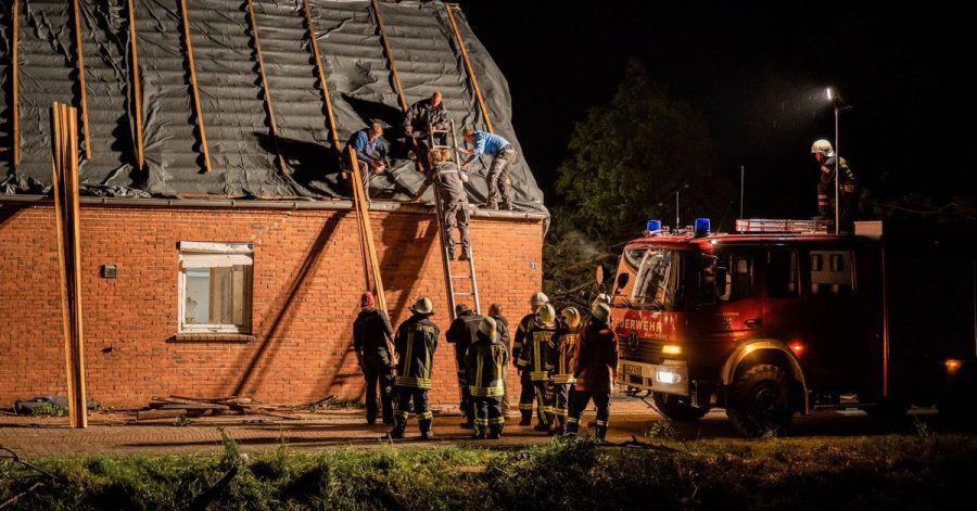 Feuerwehrleute und Helfer reparieren das Dach eines beschädigten Hauses in Berumerfehn.