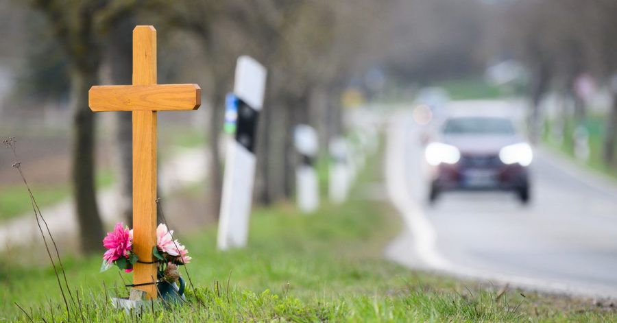 Ein Kreuz zum Gedenken an ein Opfer eines Verkehrsunfalls steht an einer Landstraße.