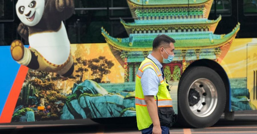 Ein Verkehrspolizist steht bei Probefahrten neben einem Bus, auf dem für den Vergnügungspark von Universal Studios geworben wird.