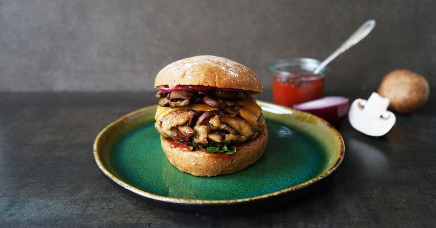 Krosse Burger aus braunen Champignons und Dinkel-Bulgur liegen zusammen mit Cheddar und roten Zwiebelringen zwischen zwei Brötchenhälften.