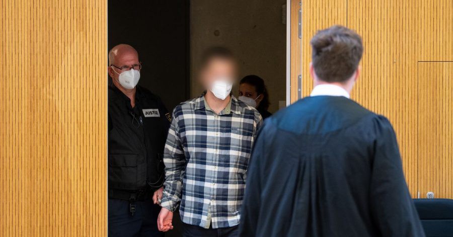 Der Angeklagte (im karierten Hemd) wird in den Sitzungssaal geführt.