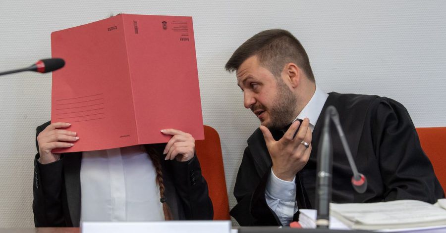 Die Angeklagte Jennifer W. hält im Gerichtssaal einen roten Aktendeckel vor das Gesicht. Rechts neben ihr sitzt Anwalt Ali Aydin.