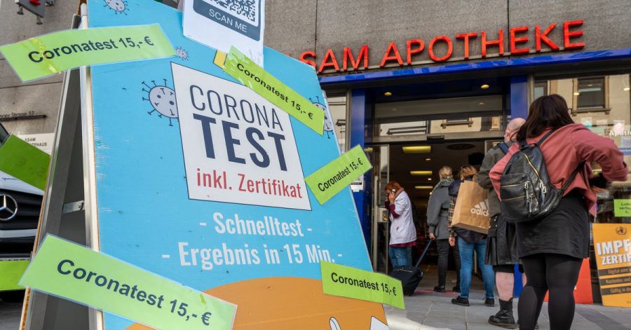 Passanten stehen in der Münchner Innenstadt vor einer Apotheke, die Coronatest für 15 Euro anbietet.