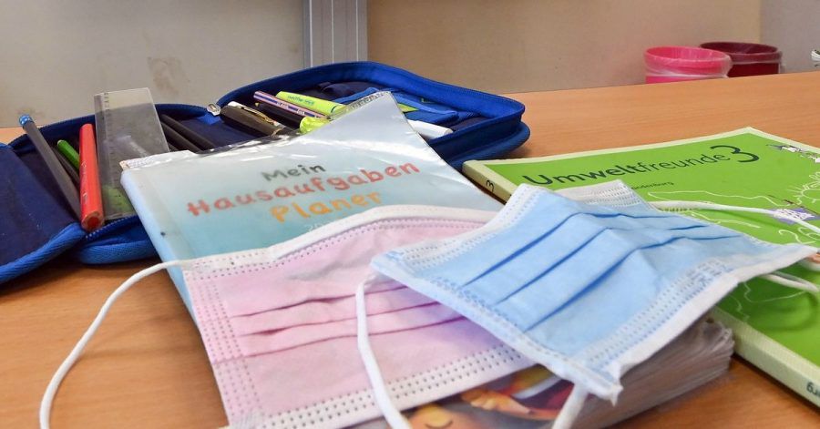 Masken liegen während einer Pause auf Arbeitsmaterialien eines Schülers in einem Klassenraum einer Grundschule.
