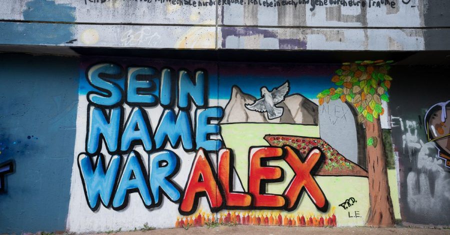 Auf einer Mauer entlang ein Graffiti "Sein Name war Alex" für den getöteten Tankstellen-Mitarbeiter gemalt.