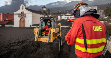 Einsatzkräfte des Militärs entfernen schwarze Asche vom Vulkan, der hinter der kleinen Kirche auf der Kanareninsel La Palma weiter Lava ausstößt.