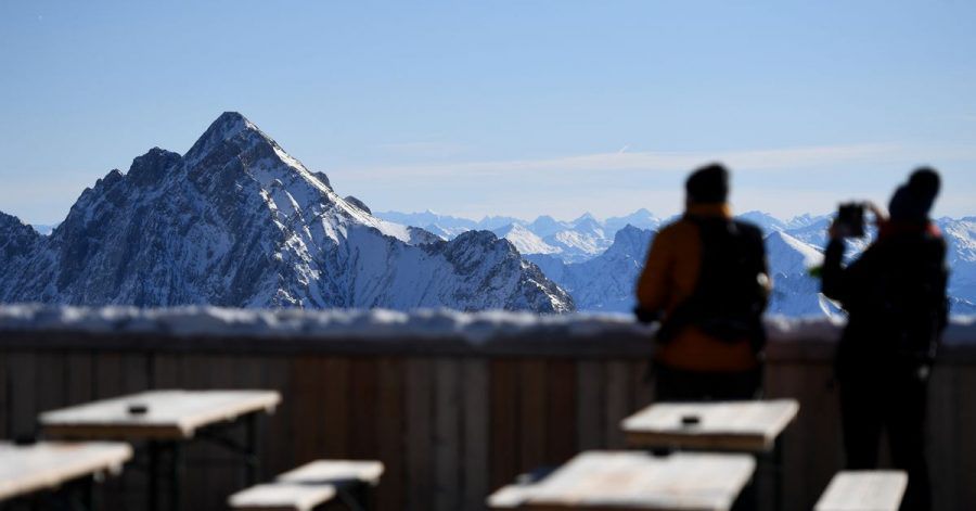 Zwei Besucher fotografieren von der Zugspitze aus das Panorama des Wettersteingebirges. Nach gut eineinhalbjähriger Pause wegen Corona sollen dort wieder Lifte laufen und Skifahrer ihre Schwünge ziehen.