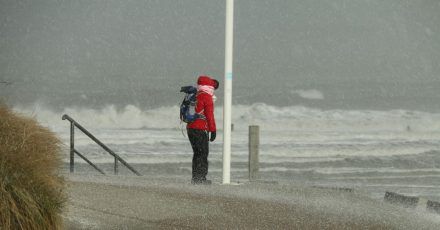 Eine Spaziergängerin auf Norderney blickt auf die Wellen der vom Sturm aufgepeitschten Nordsee.