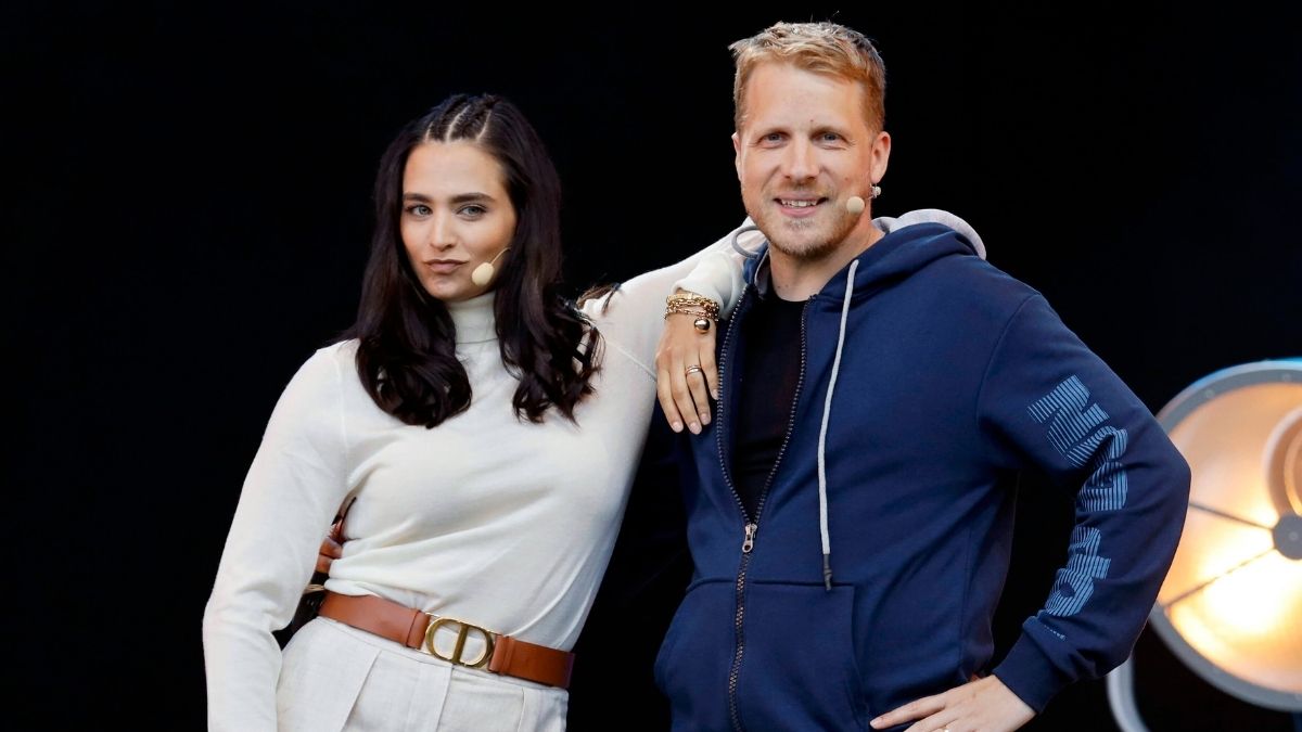 Amira Pocher in weißem Pulli lehnt an ihrem Mann Oliver Pocher im blauen Sweater" class="size-full wp-image-1377755