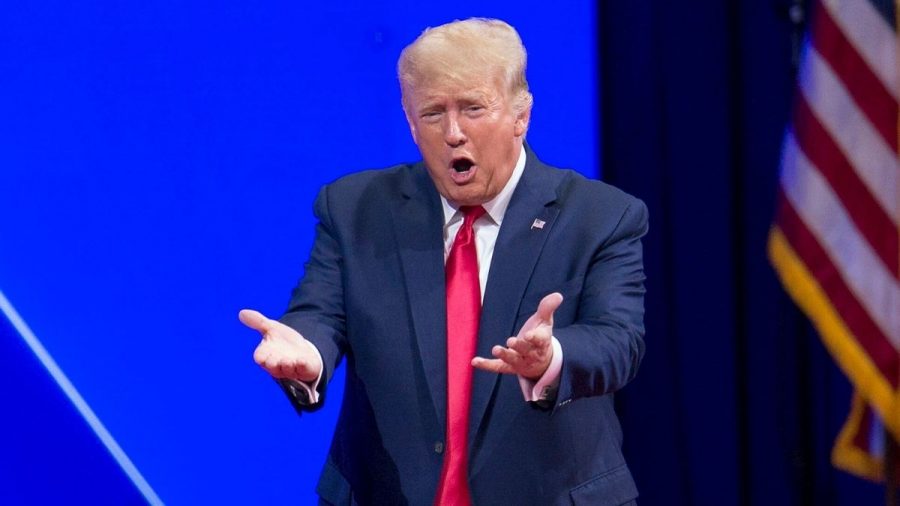 Donald Trump im Anzug mit roter Krawatte vor blauer Wand