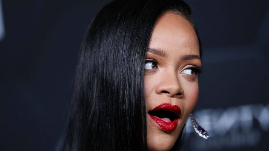 Rihanna mit rotem Lippenstift vor dunklem Hintergrund.