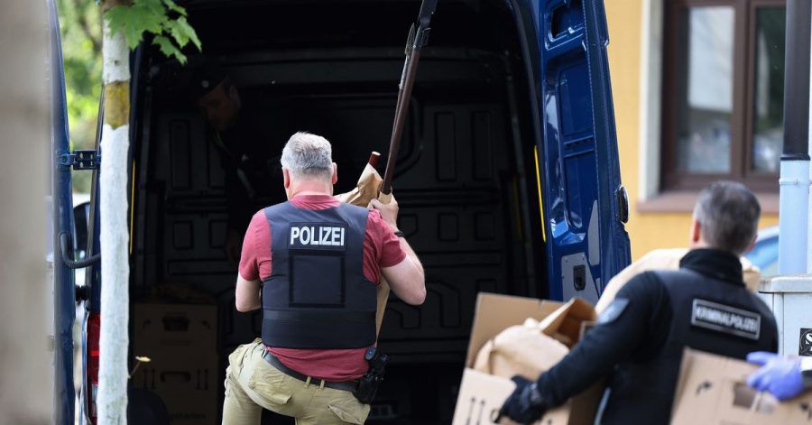 Polizisten tragen Gegenstände, darunter mehrere Stichwaffen und Speere, aus dem Wohnhaus des Verdächtigen.