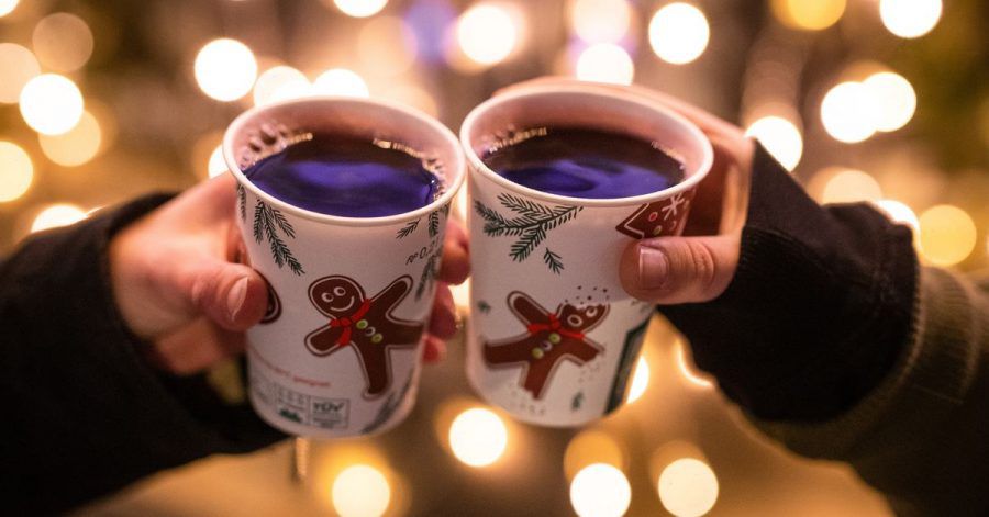 Zwei Frauen stoßen mit Glühwein in Bechern auf dem Weihnachtsmarkt an.