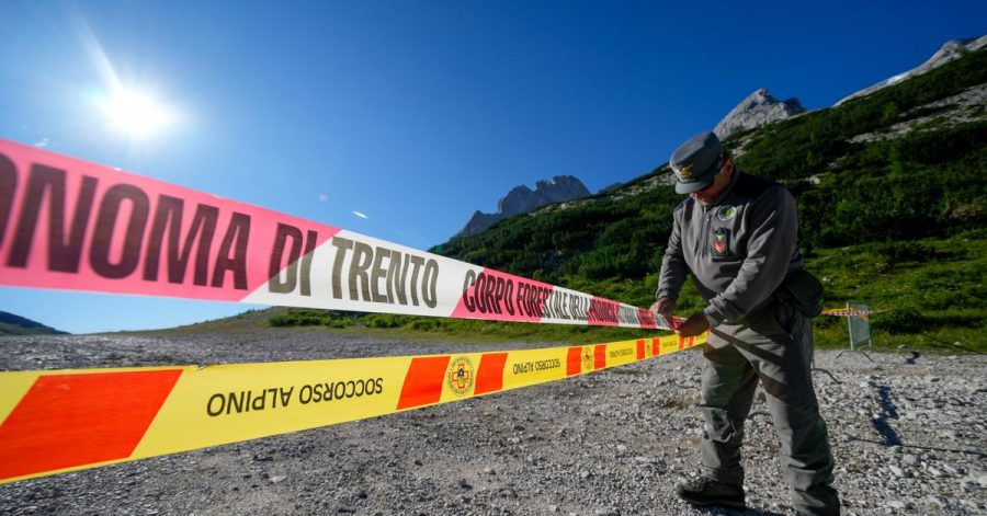 Ein Beamter der italienischen Polizei blockiert den Zugang zum Marmolata-Berg und zum Punta-Rocca-Gletscher in den italienischen Alpen mit Absperrband.