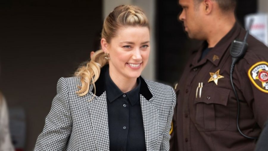 Amber Heard grinsend vor Gerichtssaal mit Polizist.