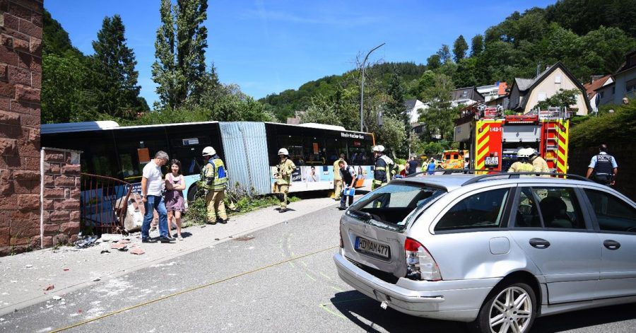 Einsatzkräfte begutachten eine Unfallstelle, an der der Linienbus gegen ein Wohnhaus gerollt ist.