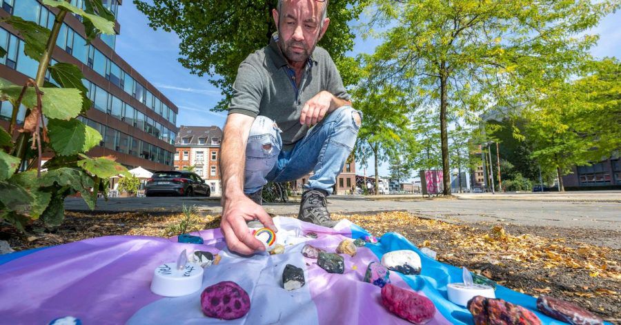 Felix Adrian Schäper vom Verein Trans*Inter*-Münster vor einer Fahne mit Gedenksteinen in Münster.