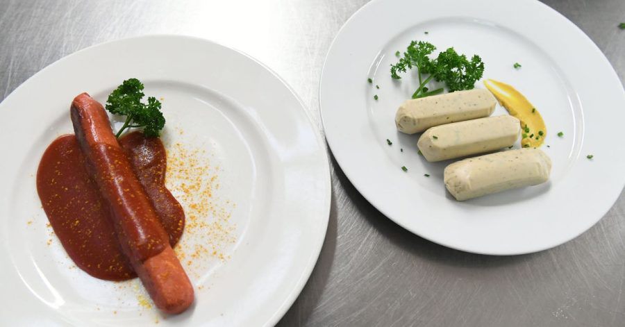 Eine vegane Currywurst und vegane Weißwürste liegen auf Tellern an der Essensausgabe im Hofbräuzelt auf dem Oktoberfest.