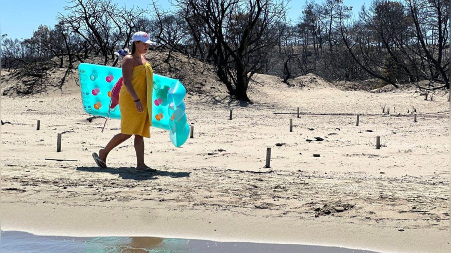 Eine Touristin am Strand von Rhodos vor verbrannter Natur. (dr/spot)